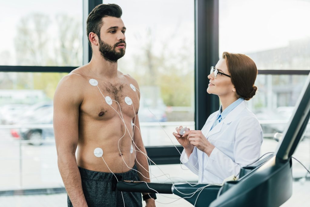 doctor conducting endurance test near sportsman with electrodes in sports center